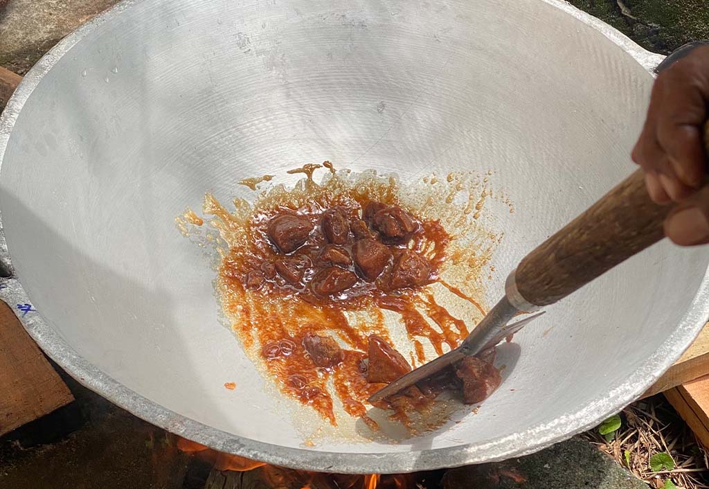 Dodol cooking in a wide pan over a wood fire, stirred with a wooden paddle